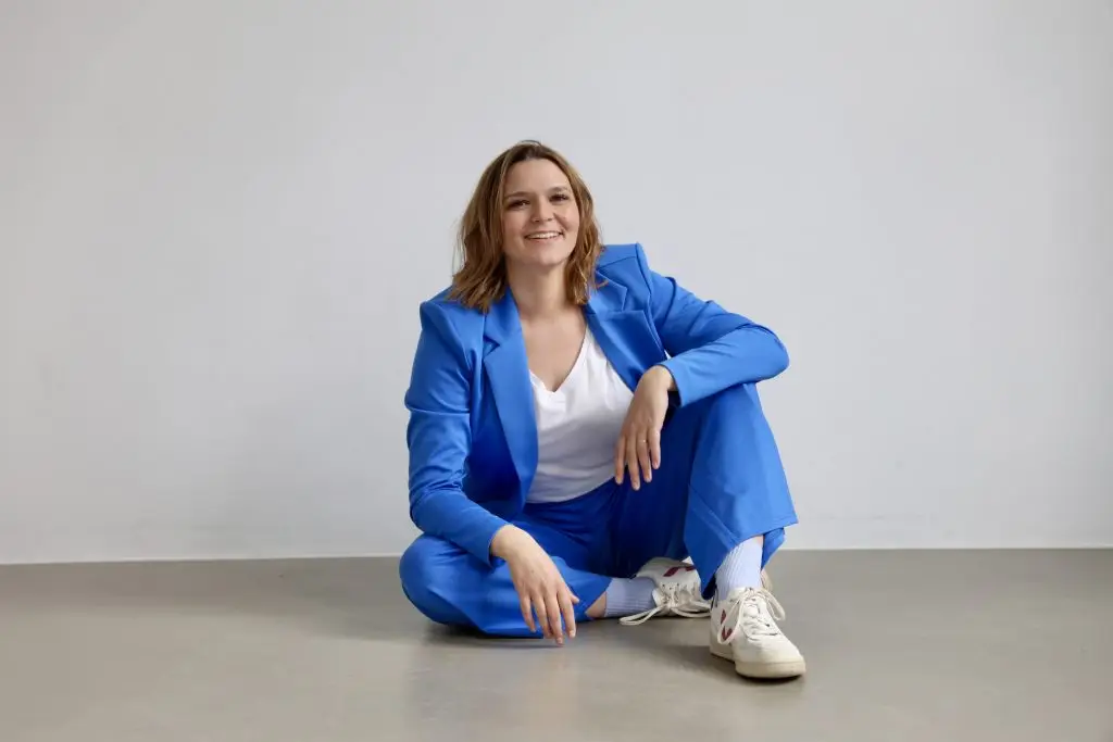 Nora Remstedt Expertin für Bunroutprävention sitzt lächend auf dem Boden in einem blauen Anzug