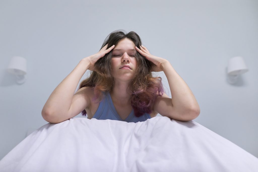 Frau von unten Fotografiert, mann kann die Decke und den Oberkörper sehen, sie sitzt und hält sich den Kopf, hat durch Stress Schwindel bekommen, ihre Haare sind offfen.