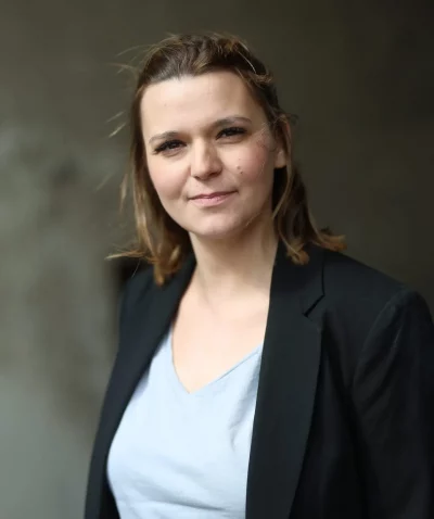 Workshopleiterin Nora Remstedt steht draußenen mit einer schwarzem n blazer und schaut in die Kamera , ihre Harre sind halboffen.